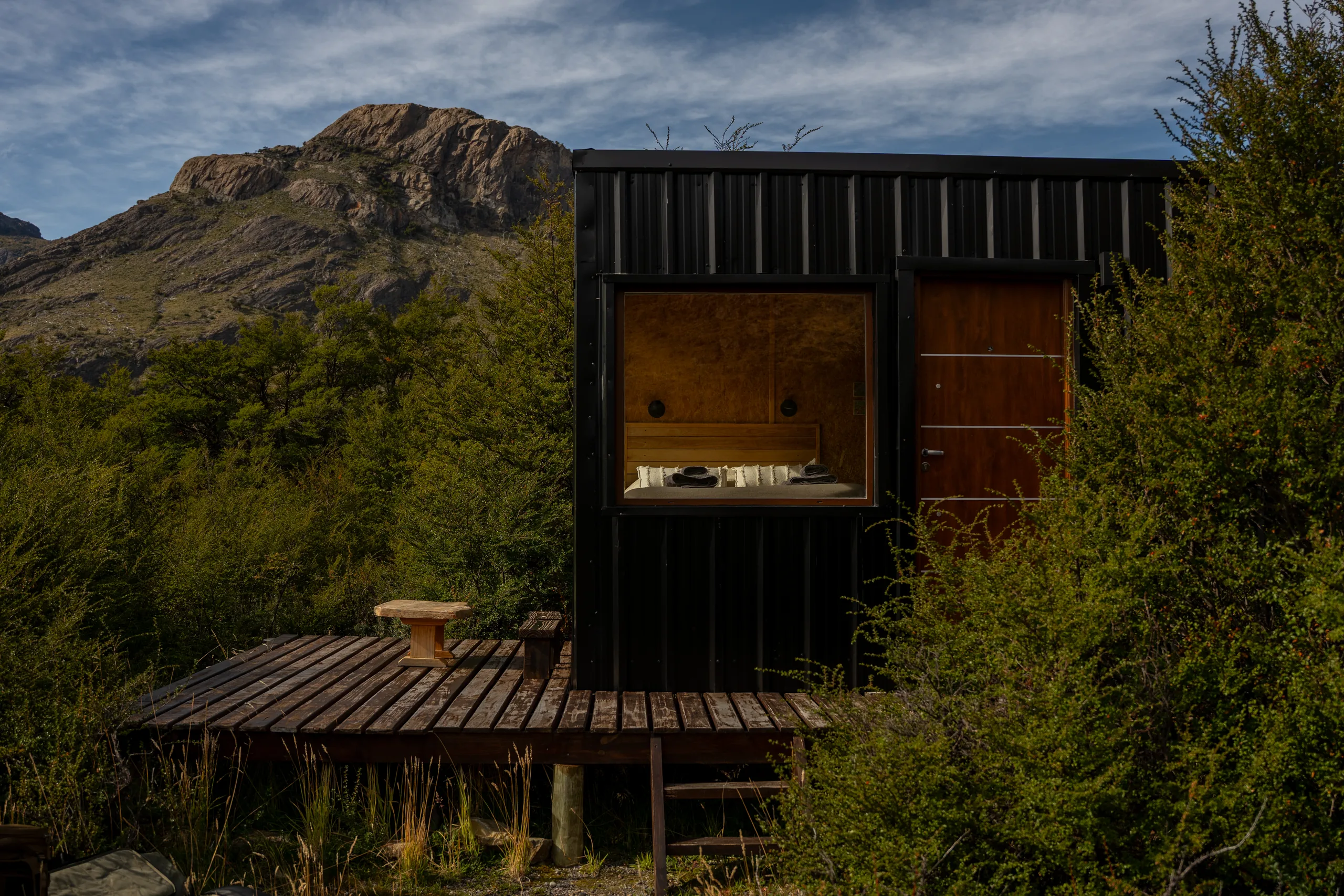 Una de las tiny houses de Cerro Eléctrico con su deck, en medio del bosque, con la cama a la vista por el ventanal
